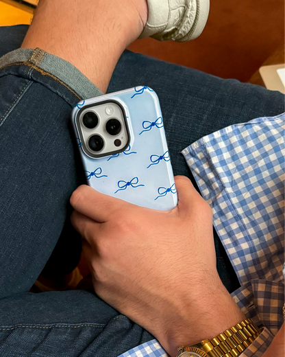 Person holding a phone with a blue case featuring navy blue bows on it.