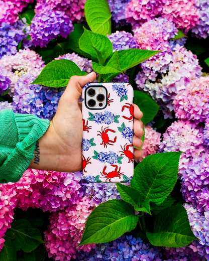 Hand holding a phone case with crabs and hydrangeas design against a background of hydrangea flowers